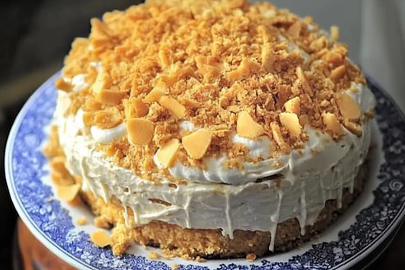 A whole Blum's Coffee Crunch Cake displayed on a decorative plate, featuring layers of whipped cream and golden coffee crunch topping. Title: Blum's Coffee Crunch Cake on Decorative Plate